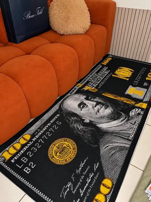 Tapis billet de 100 dollars noir et or posé devant un canapé orange