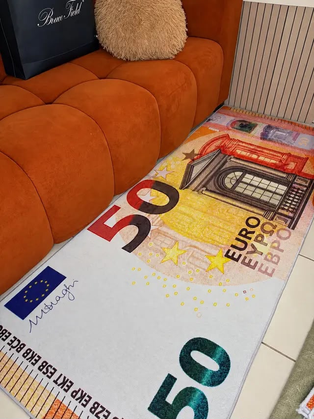 Tapis billet de 50 euros orange et jaune posé devant un canapé